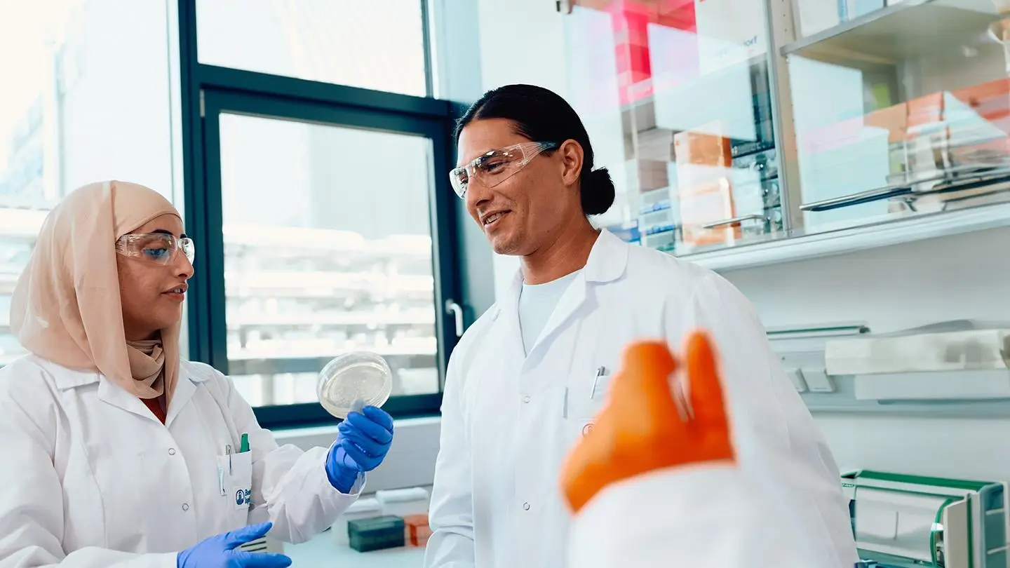 researcher sitting at microscope greeting colleague