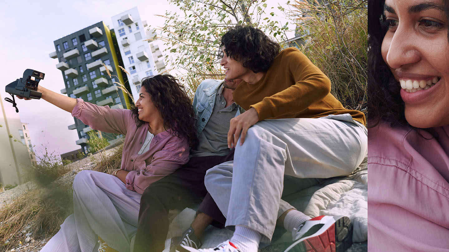 Trois amis souriant et s'amusant à prendre un selfie à l'aide d'une caméra instantanée dans un parc.