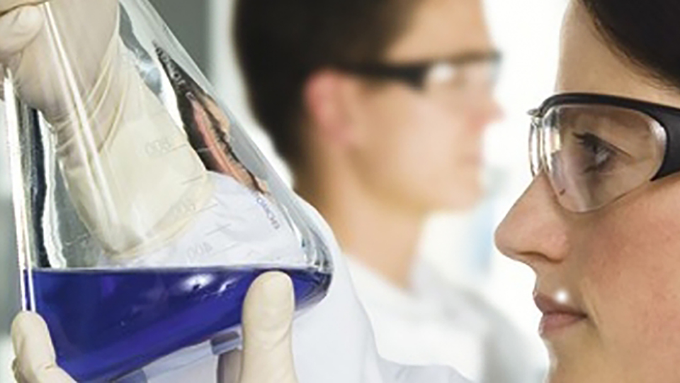 A woman holds and looks into a conical flask with a blue liquid in it