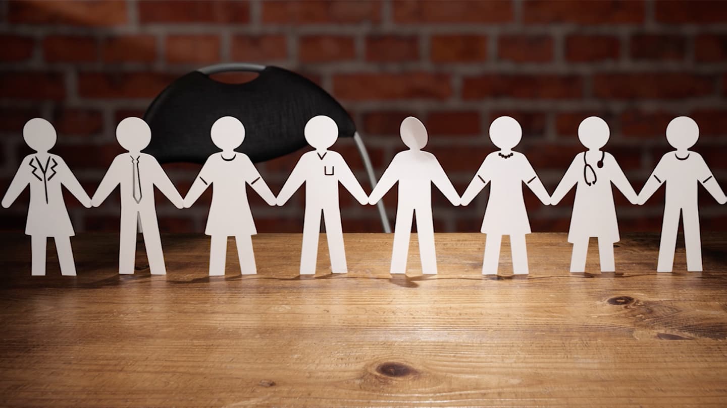 Paper cut outs of eight people joined together at the hands on a desk