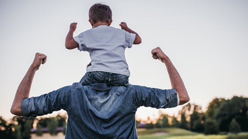 View from behind of son sitting on father's shoulders walking